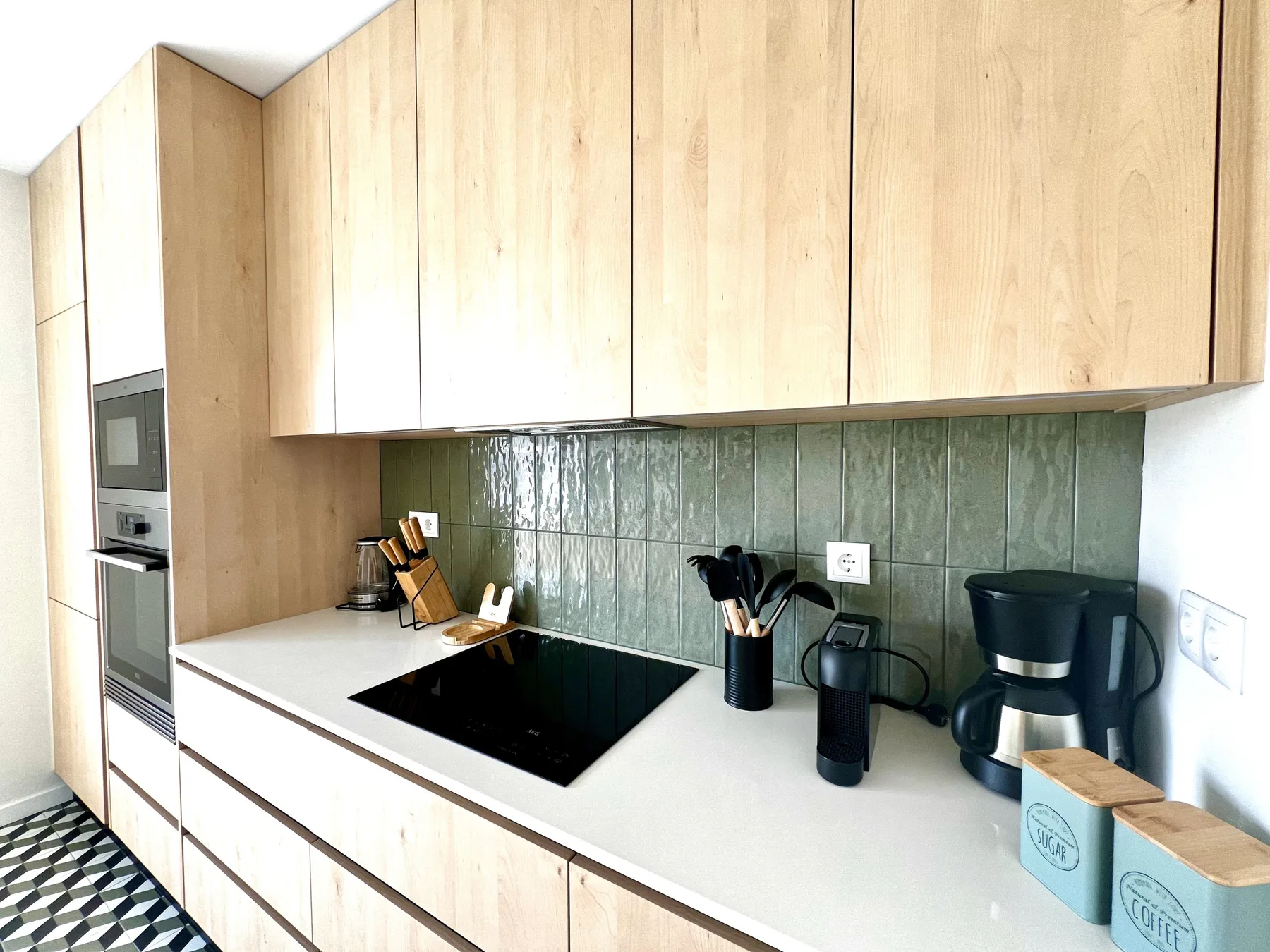Una cocina moderna con gabinetes de madera clara, una placa de cocina y electrodomésticos sobre la encimera.