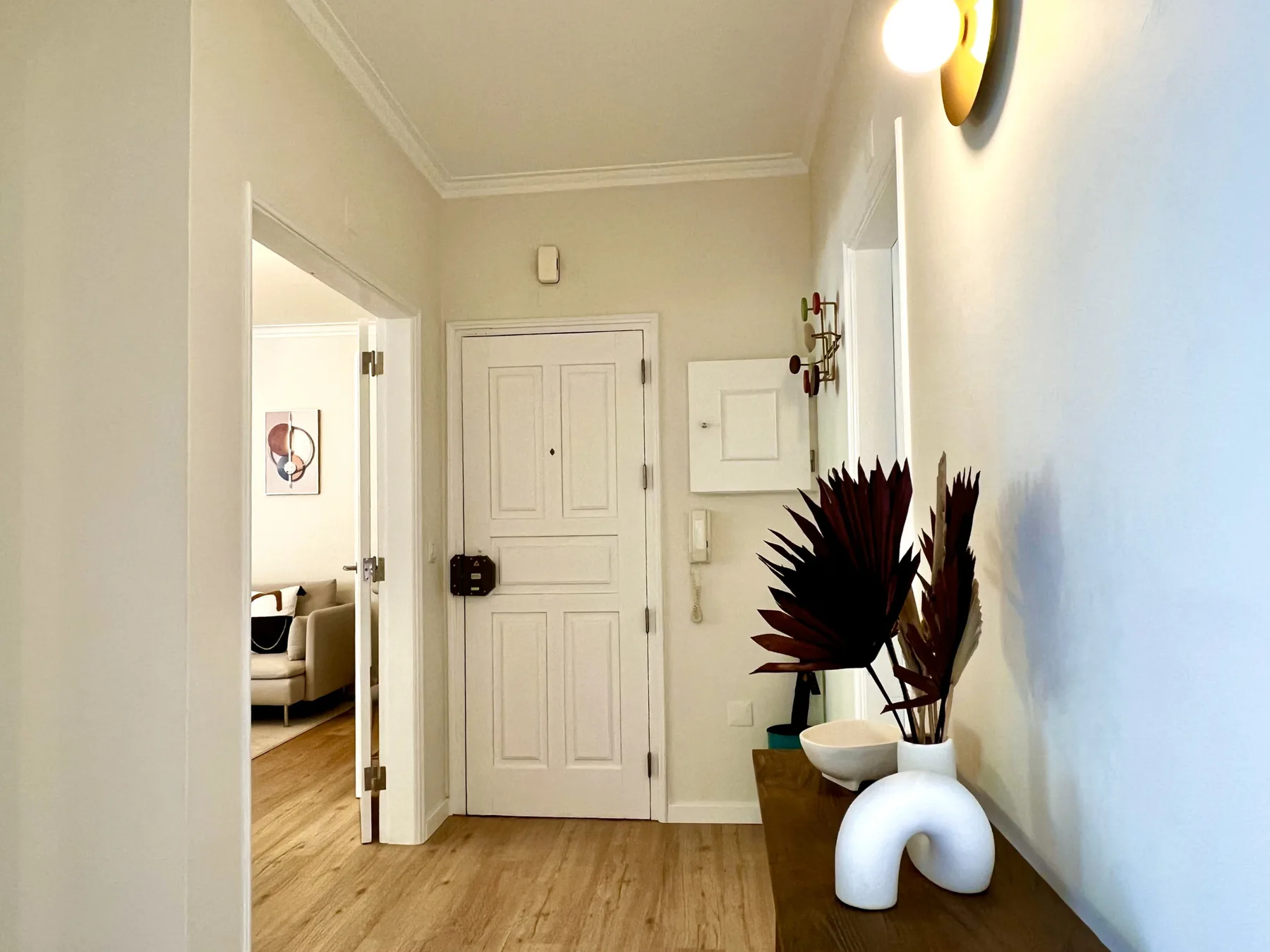 La entrada de un apartamento con una puerta principal, una mesa consola y plantas decorativas.