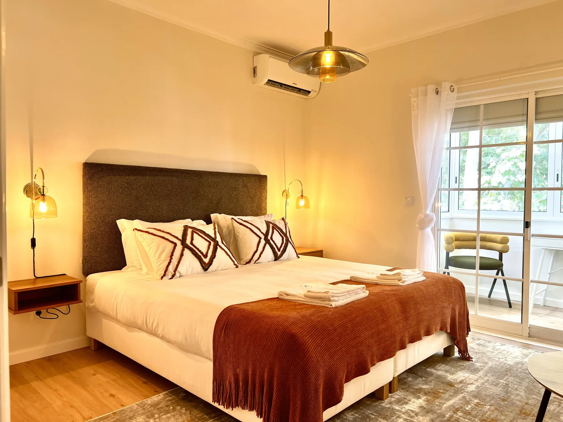 Dormitorio con una cama grande, cojines estampados y una puerta corrediza de vidrio.