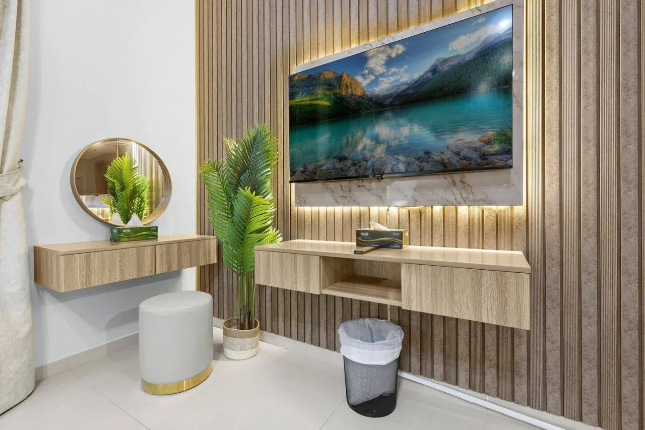 A modern vanity area features a wall-mounted television and a round mirror.