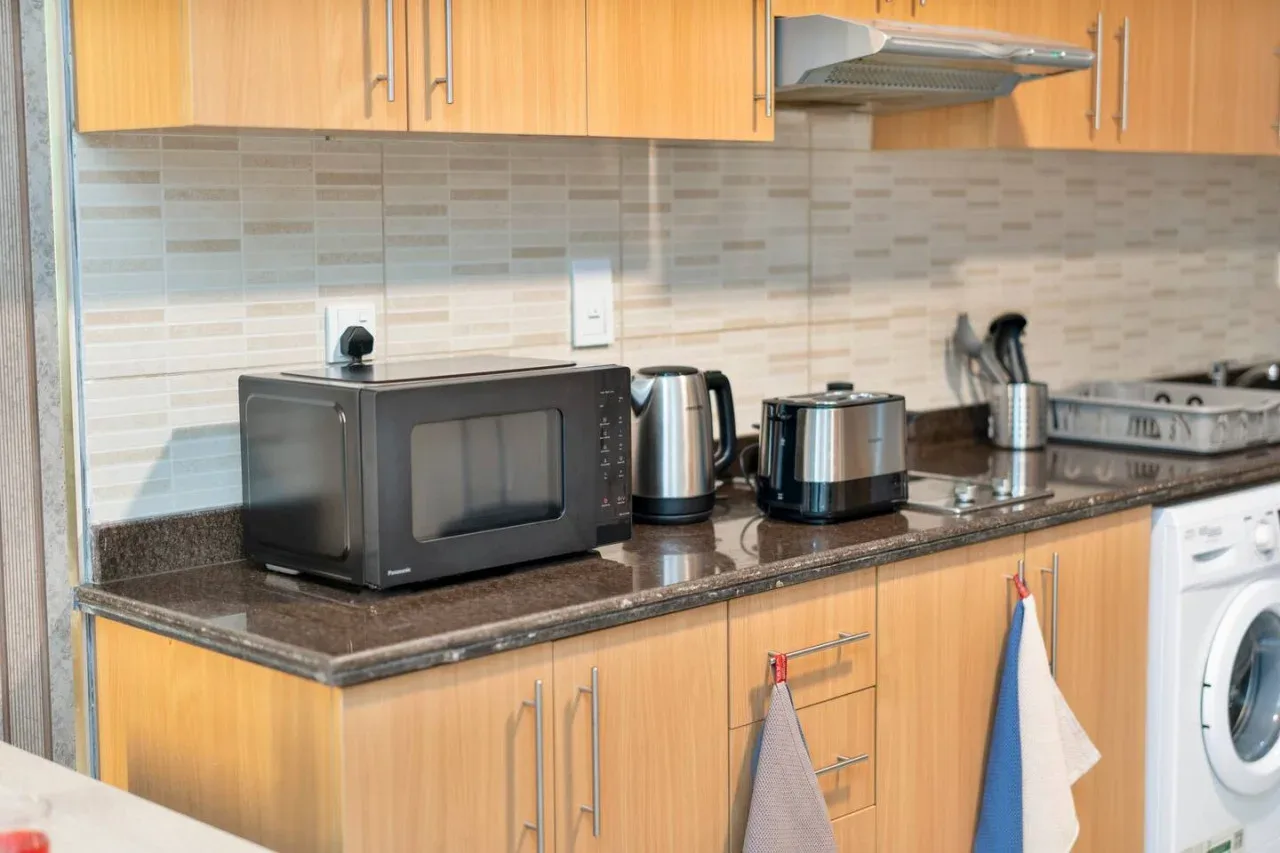 A kitchen counter with a microwave, kettle, toaster, and washing machine.