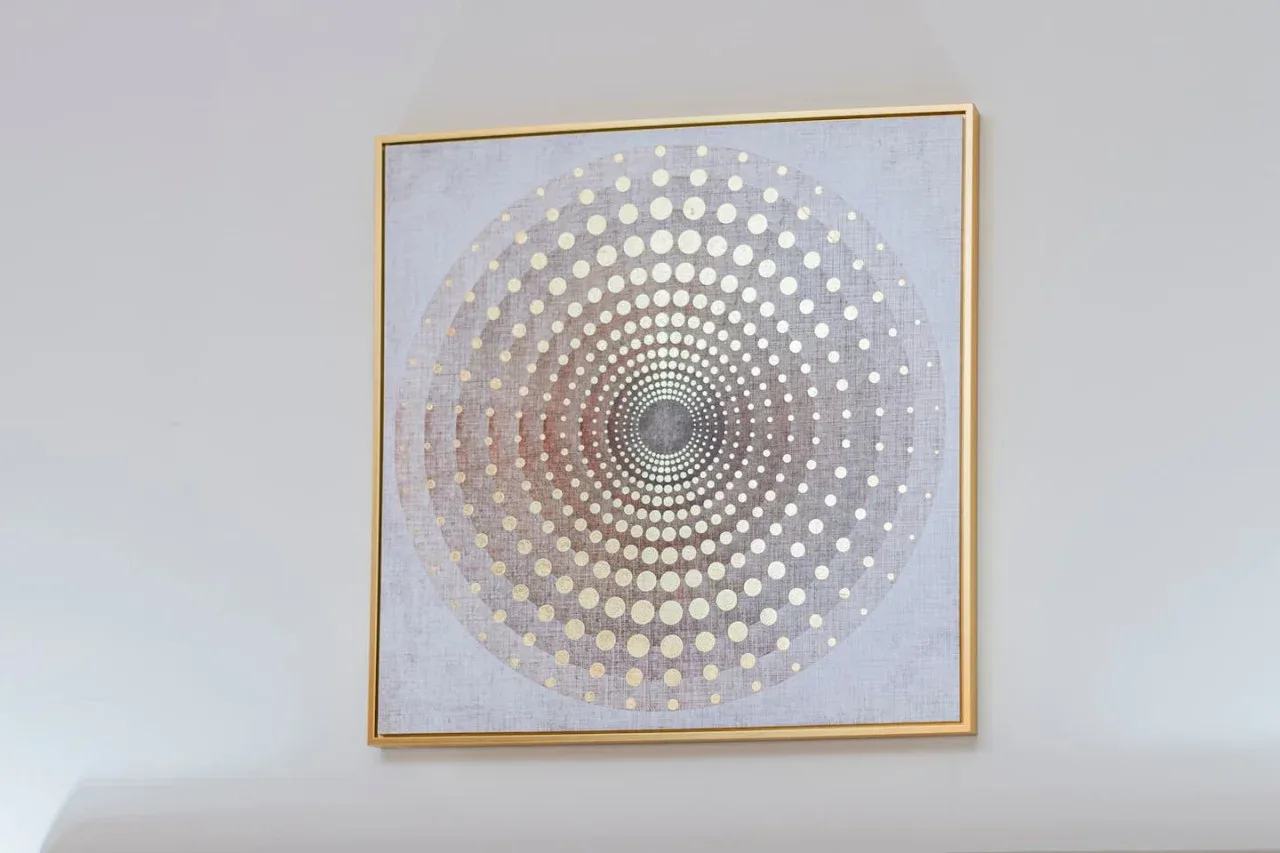 A framed circular geometric artwork hangs on a light-colored wall.
