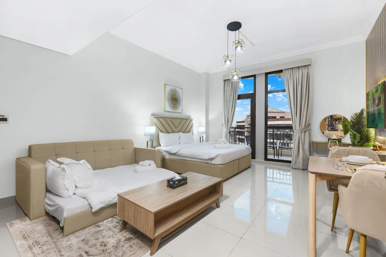 A bright bedroom with two beds, a wooden coffee table, and glass doors opening to a balcony.