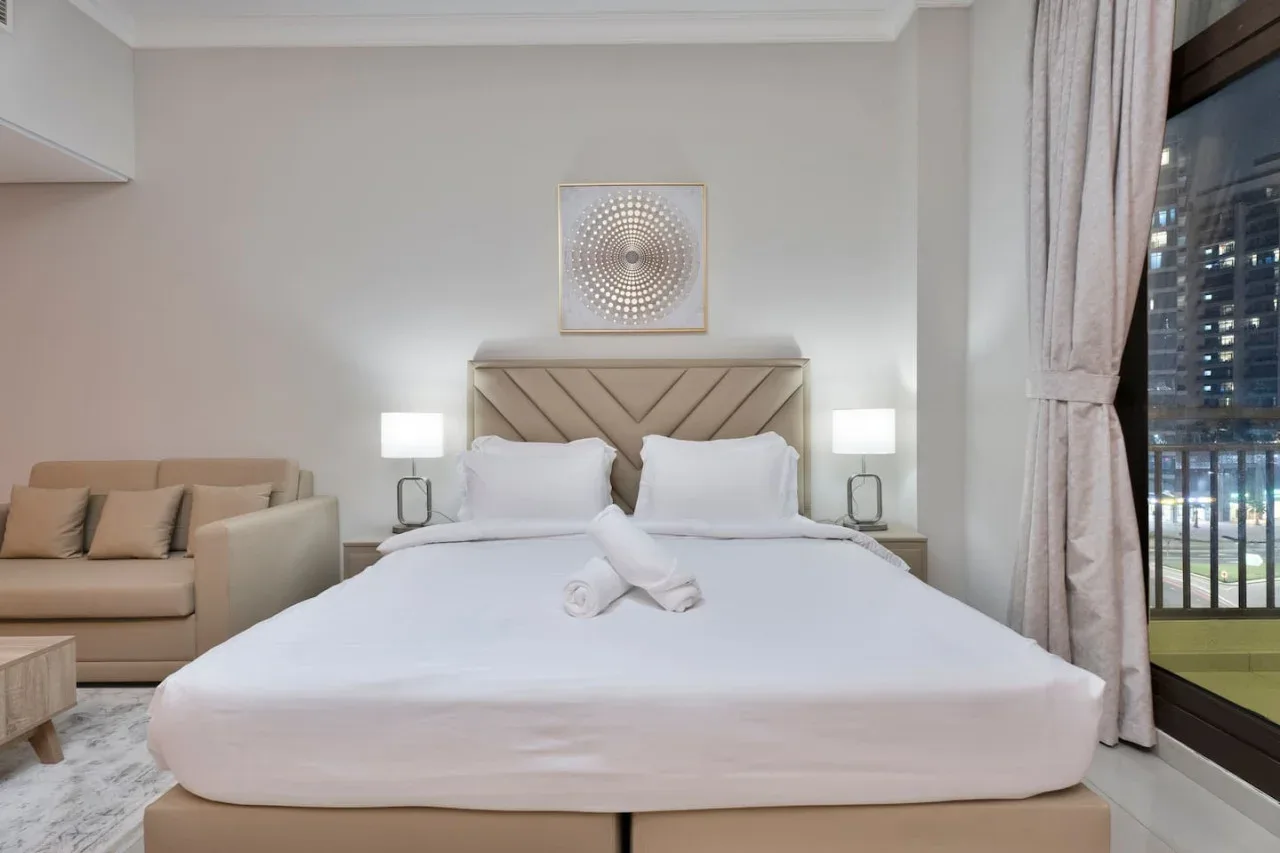 A bedroom with a neatly made bed and a small seating area.