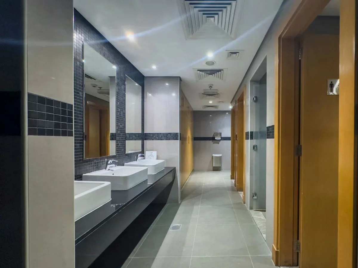 A tiled restroom corridor with sinks along the wall and doors on either side.