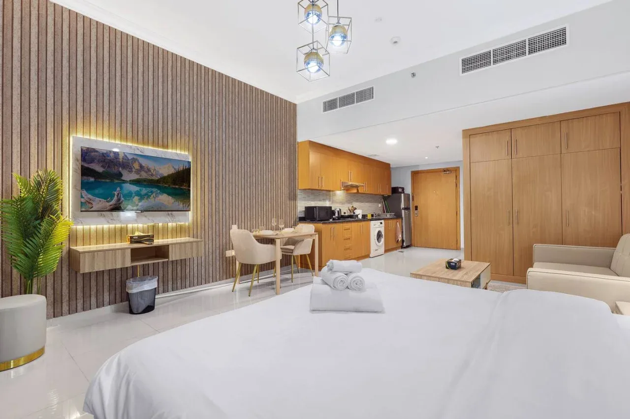 A bright bedroom with a bed, seating area, and compact kitchen.