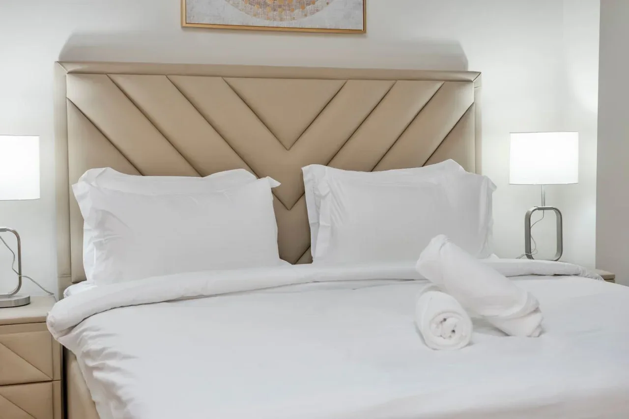 A neatly made bed with white bedding and a geometric upholstered headboard.