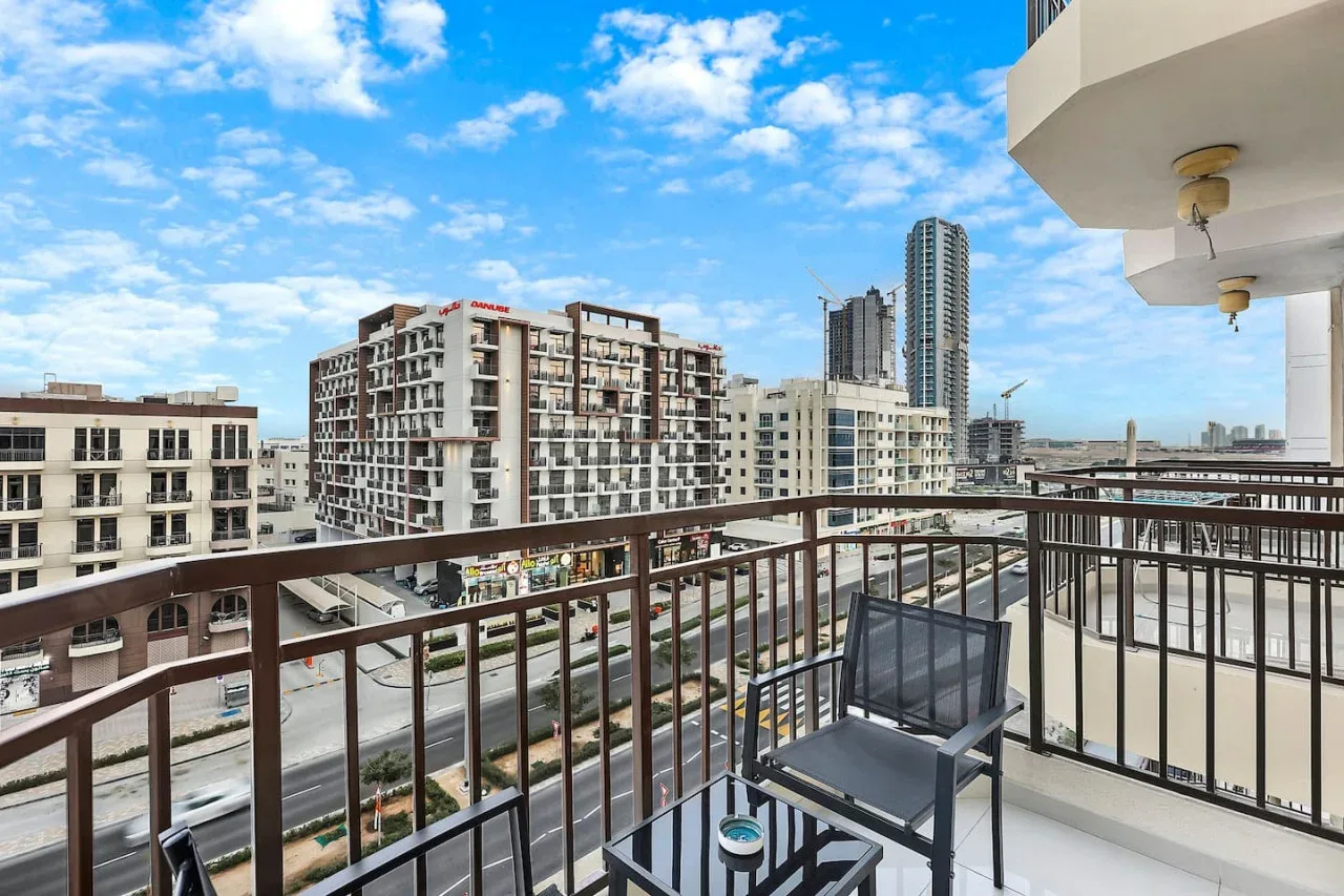 A balcony overlooks nearby buildings, with outdoor seating beside the railing.