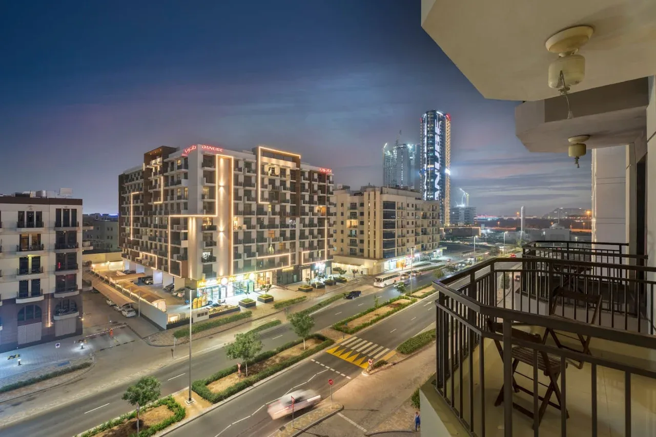 A city street at dusk, viewed from a balcony overlooking illuminated buildings.