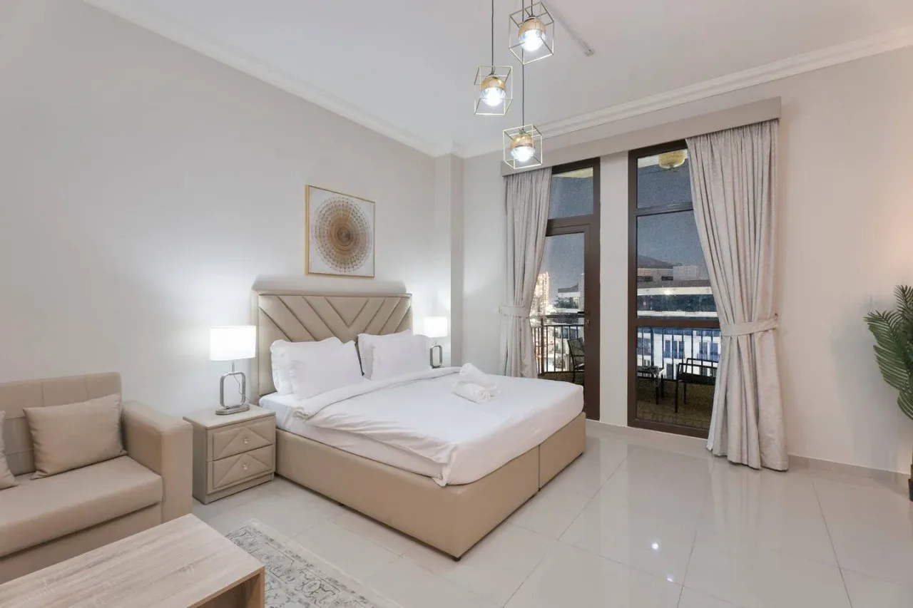 A bright bedroom with a large bed and tall windows opening onto a balcony.