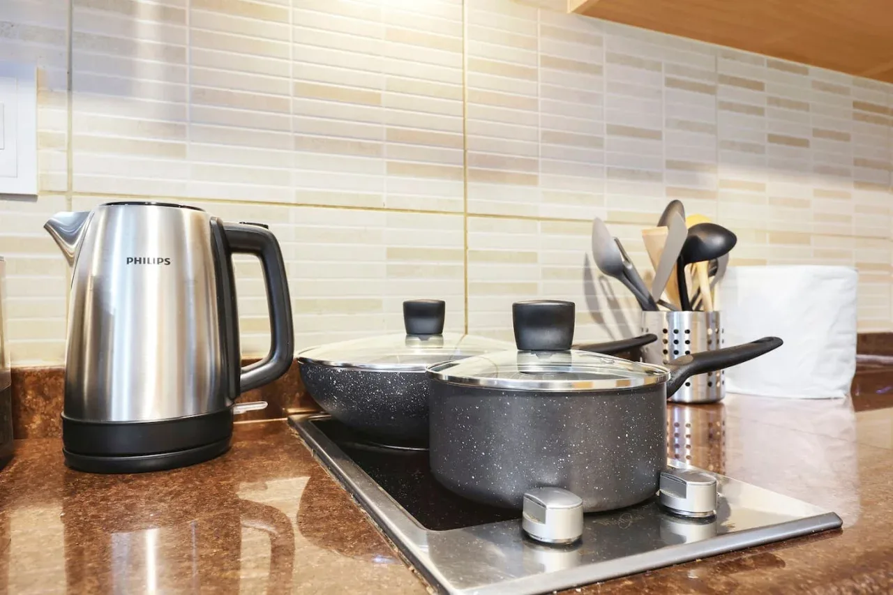 A kitchen countertop with a kettle, cookware, and cooking utensils.