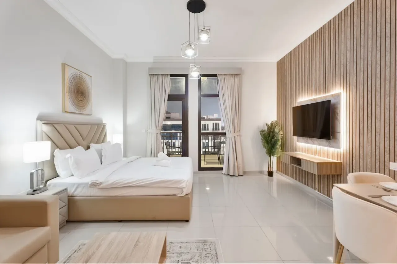 A bright bedroom with a bed, tall windows, and a wall-mounted television.