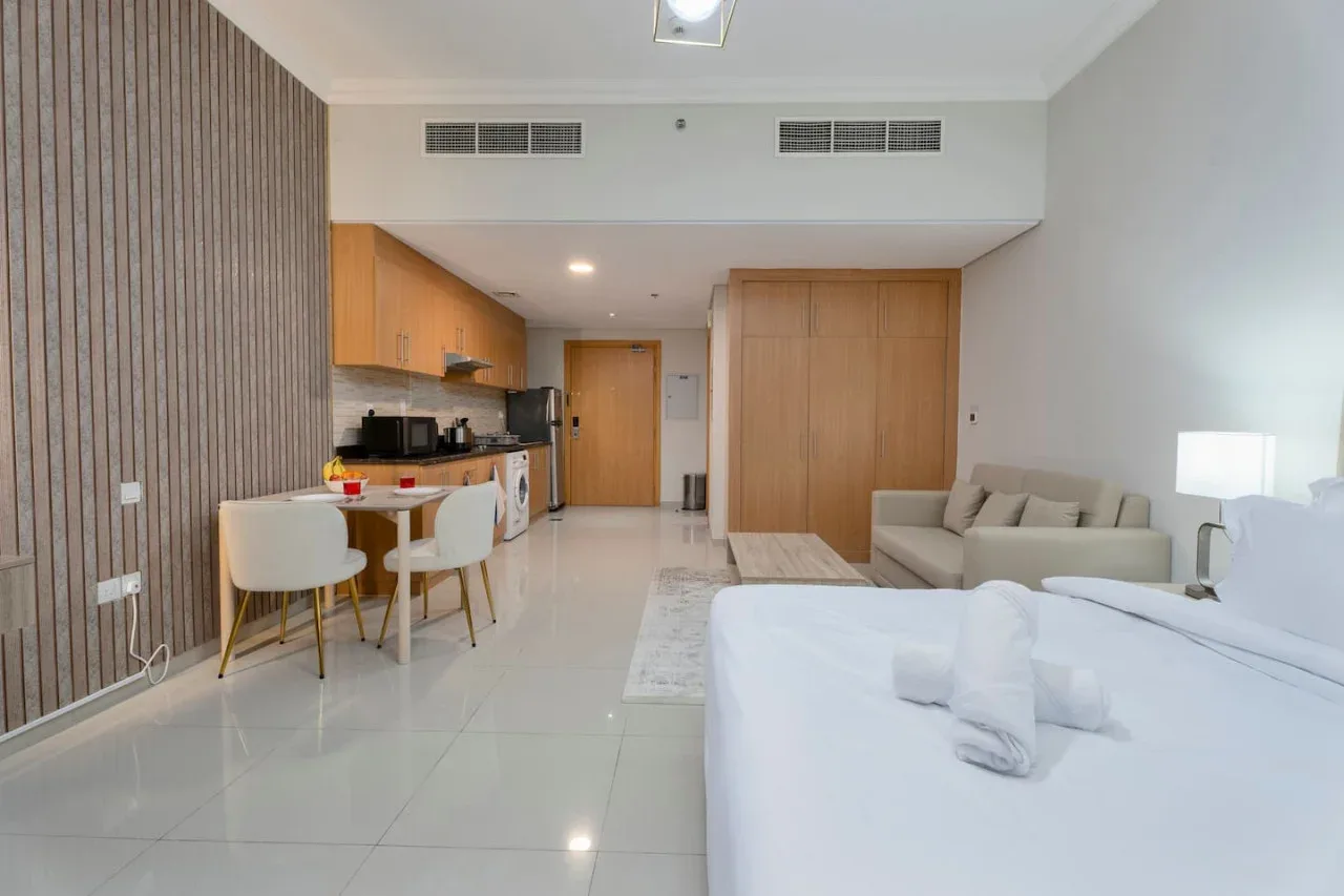 A bright studio room combines a kitchenette, dining table, seating, and a bed.