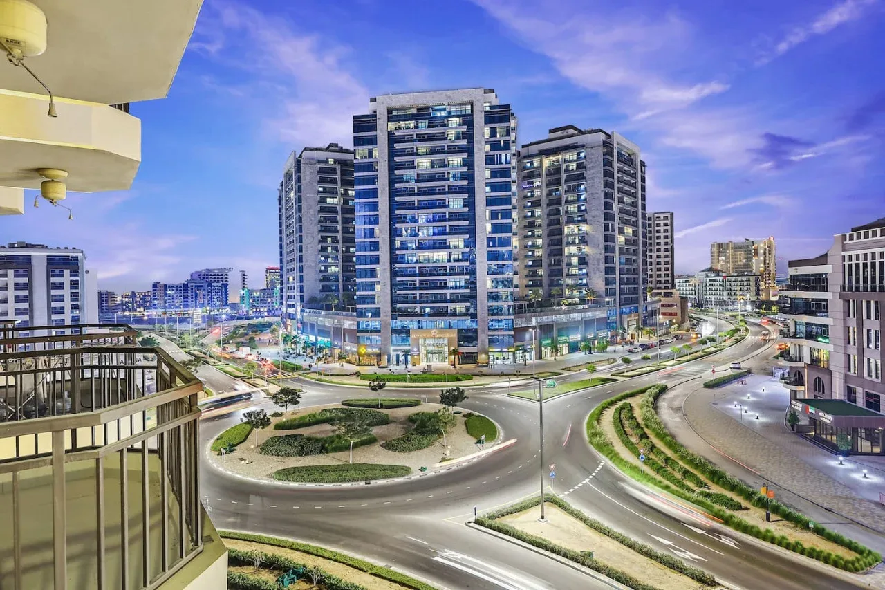 A city intersection curves around landscaped traffic islands beneath modern high-rise buildings.