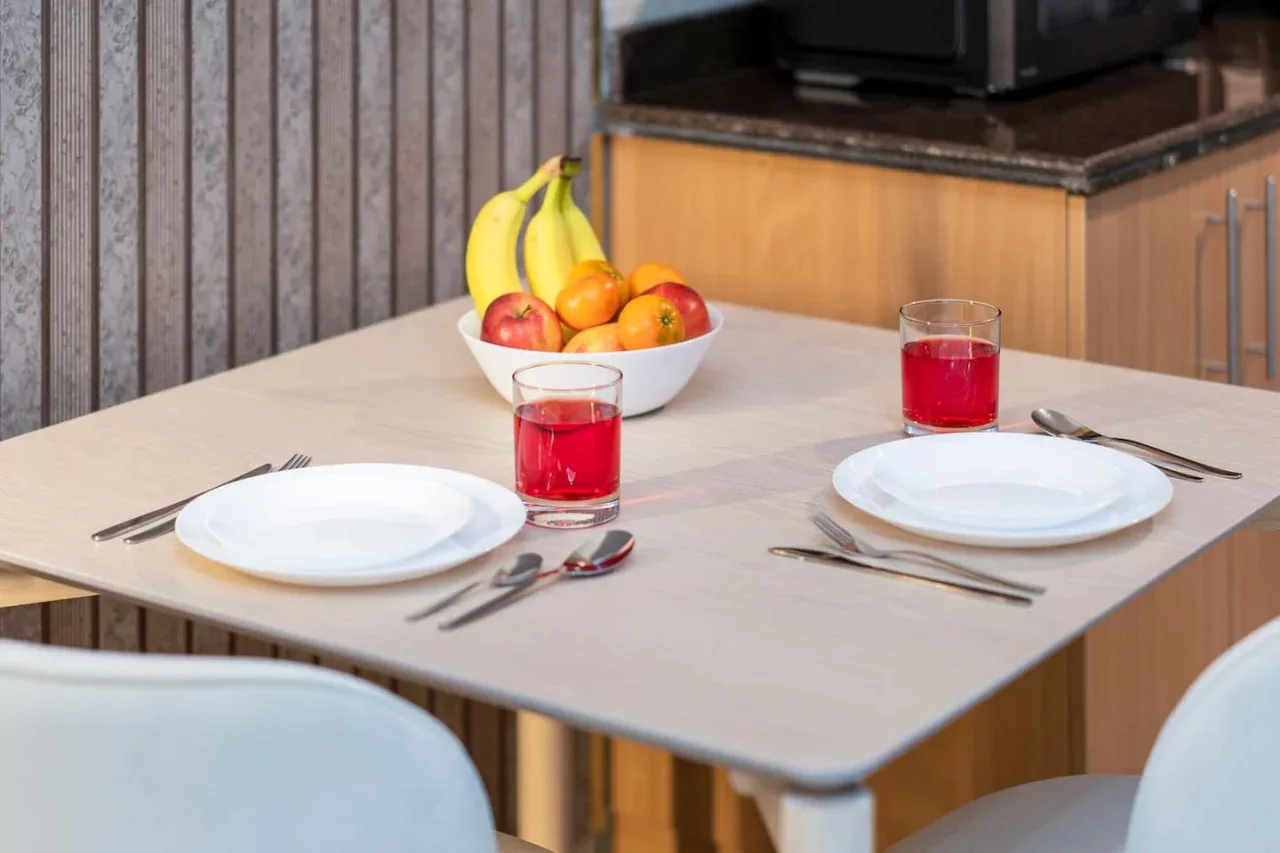 A dining table is set with plates, red drinks, and a bowl of fruit.