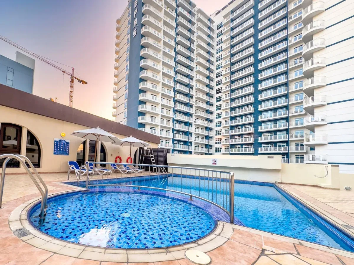 A swimming pool with a circular section sits beside a tall apartment building.