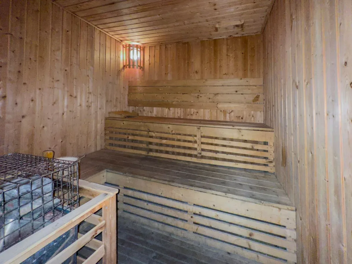 A wood-paneled sauna room with tiered wooden seating and a small wall light.
