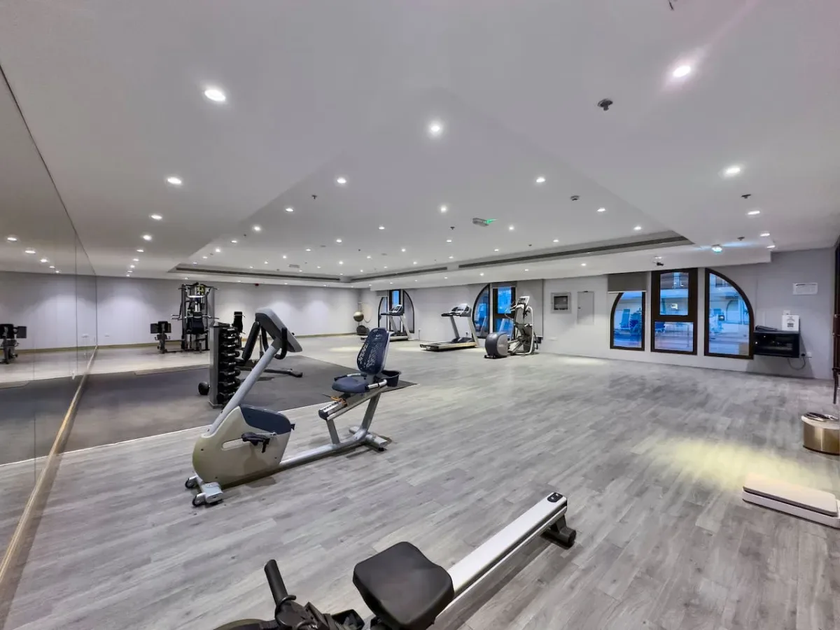 A spacious gym with exercise machines, weight benches, and a mirrored wall.