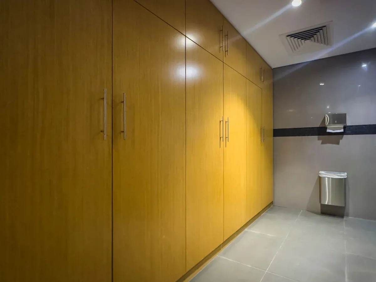 A tiled washroom with wooden storage cabinets and wall-mounted dispensers.