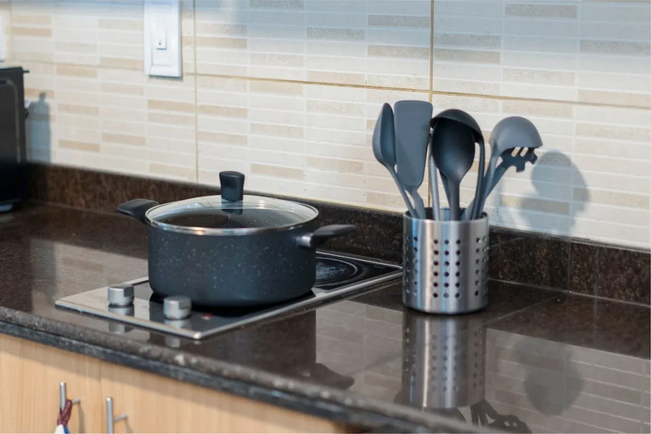 A kitchen cooktop with a covered pot and cooking utensils on the counter.