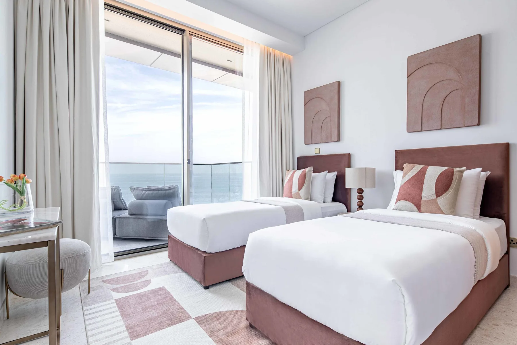 Un dormitorio luminoso con dos camas junto a grandes ventanales con vistas al agua.