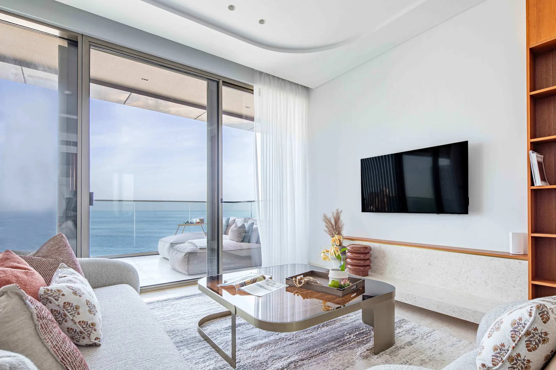 Sala de estar con televisión y puertas de vidrio con vista al mar.