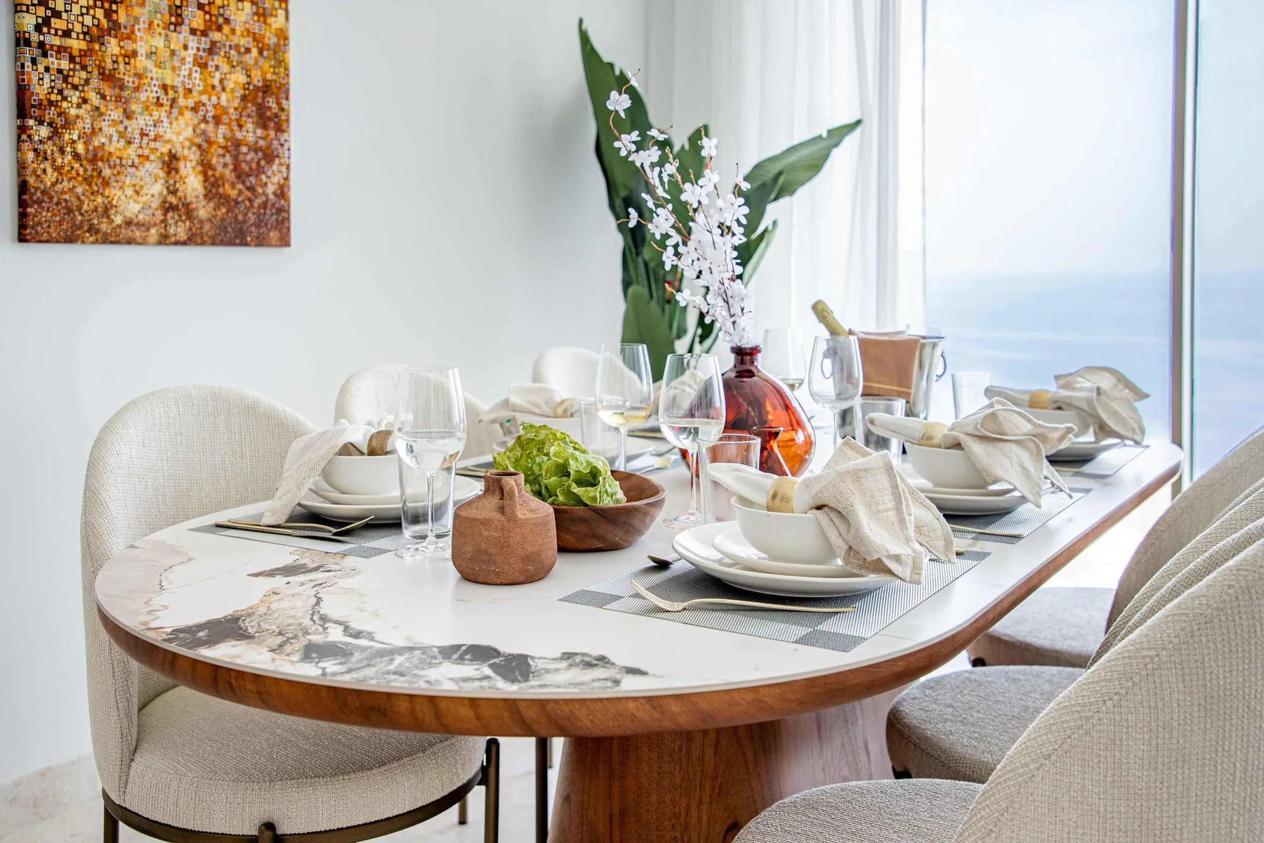 Una mesa de comedor está puesta con vajilla, copas y un jarrón con flores.