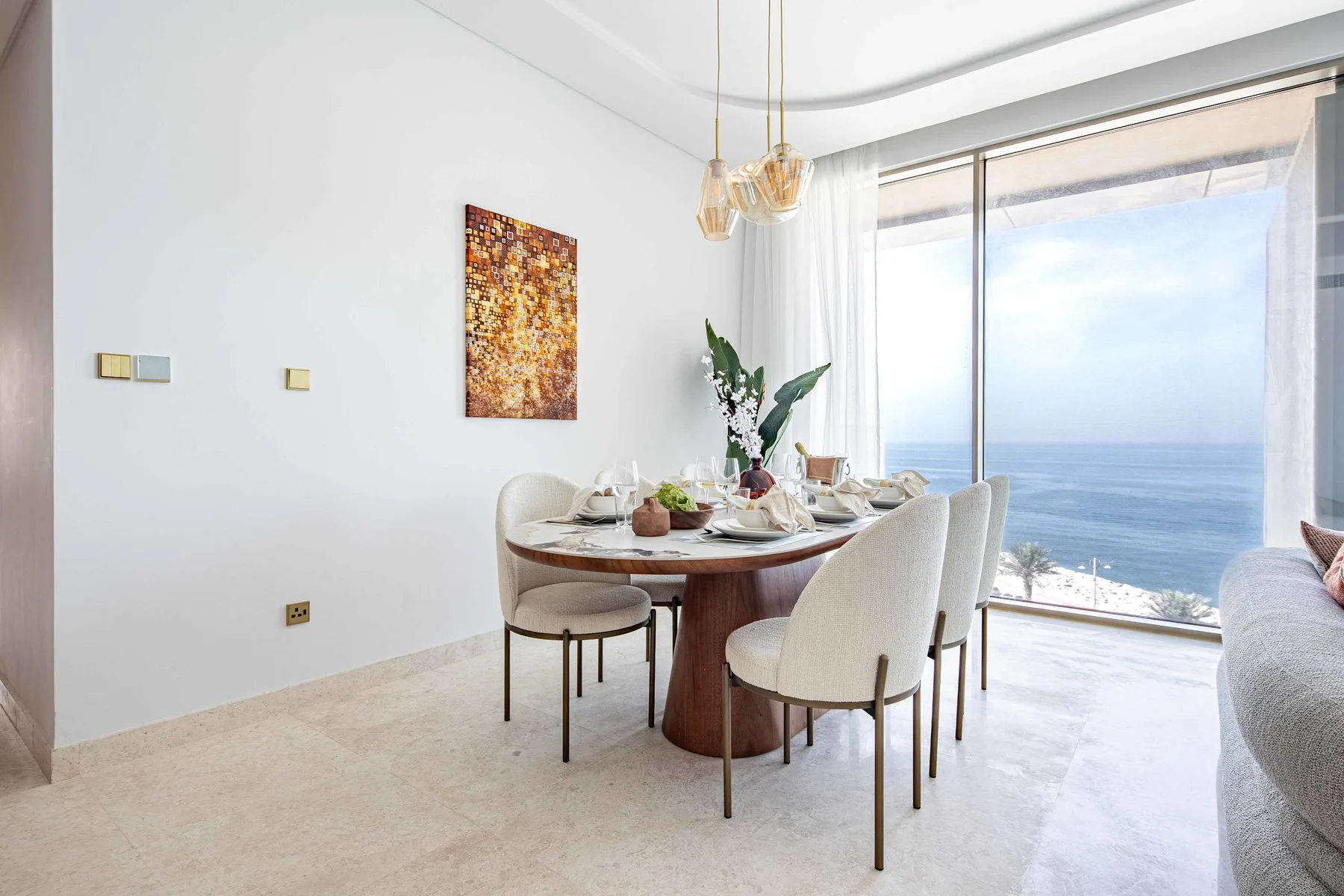 Comedor con la mesa puesta junto a grandes ventanas con vistas al mar.
