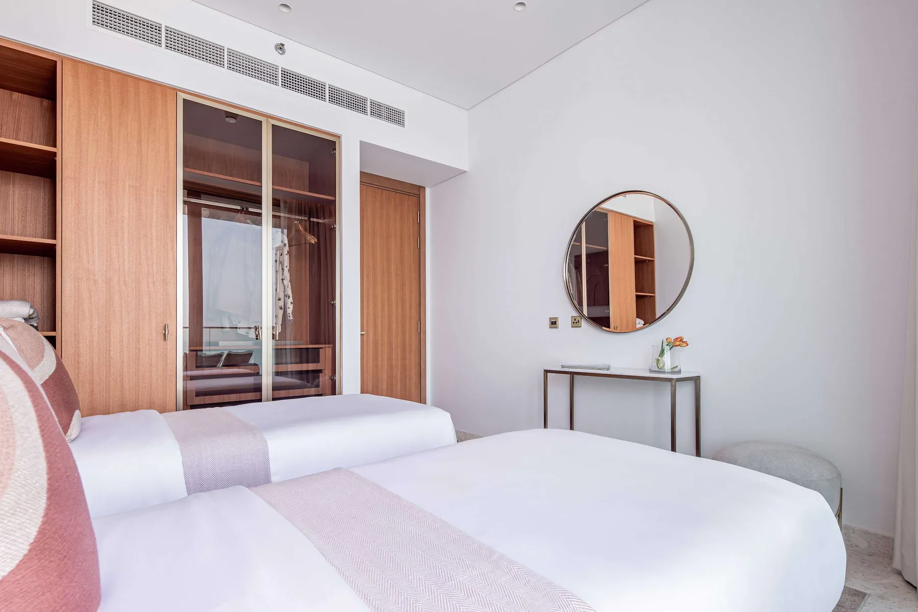 Un dormitorio luminoso con camas, armarios de madera y un espejo redondo en la pared.