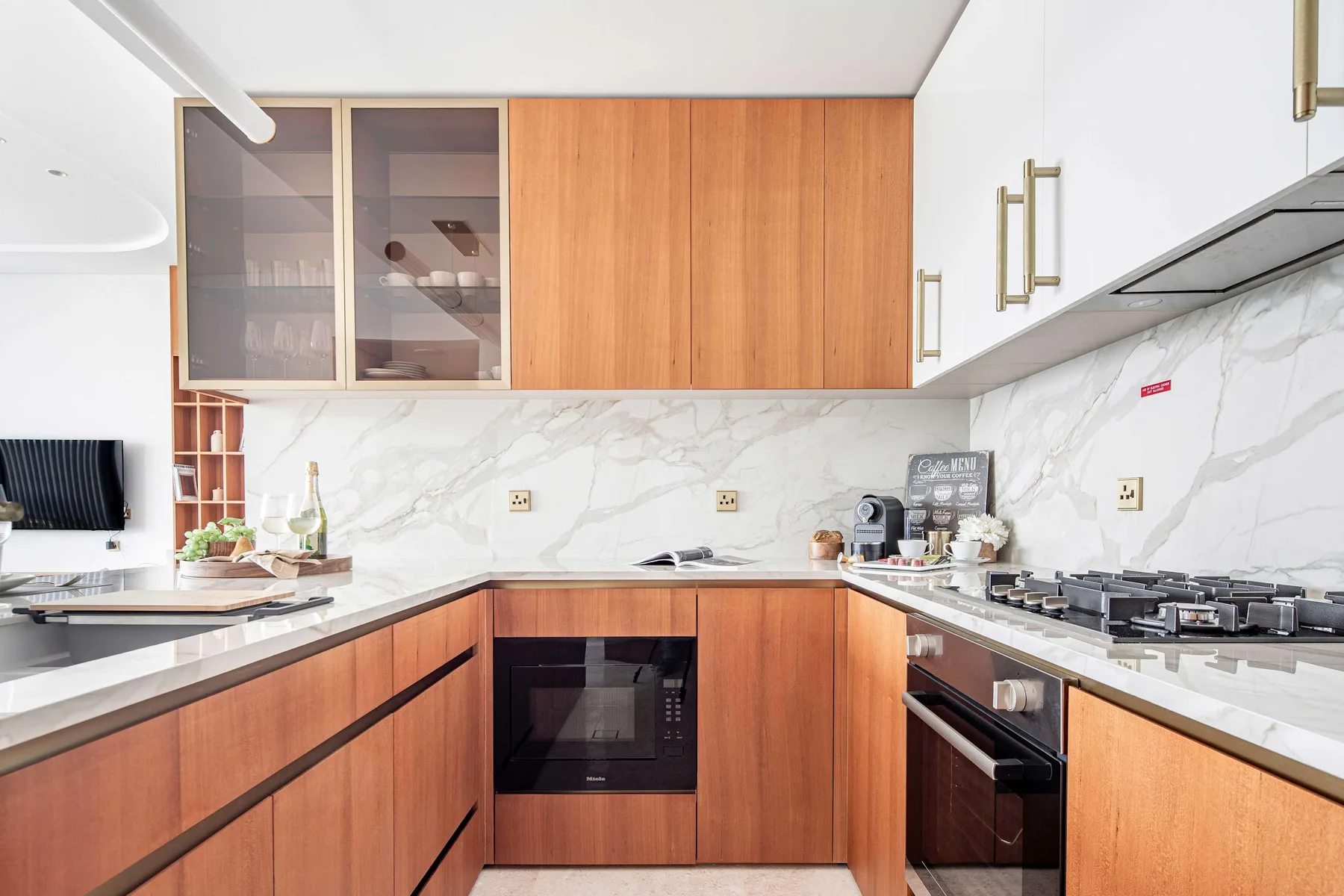 Una cocina moderna con gabinetes de madera, paredes con vetas marmoleadas y electrodomésticos sobre la encimera.