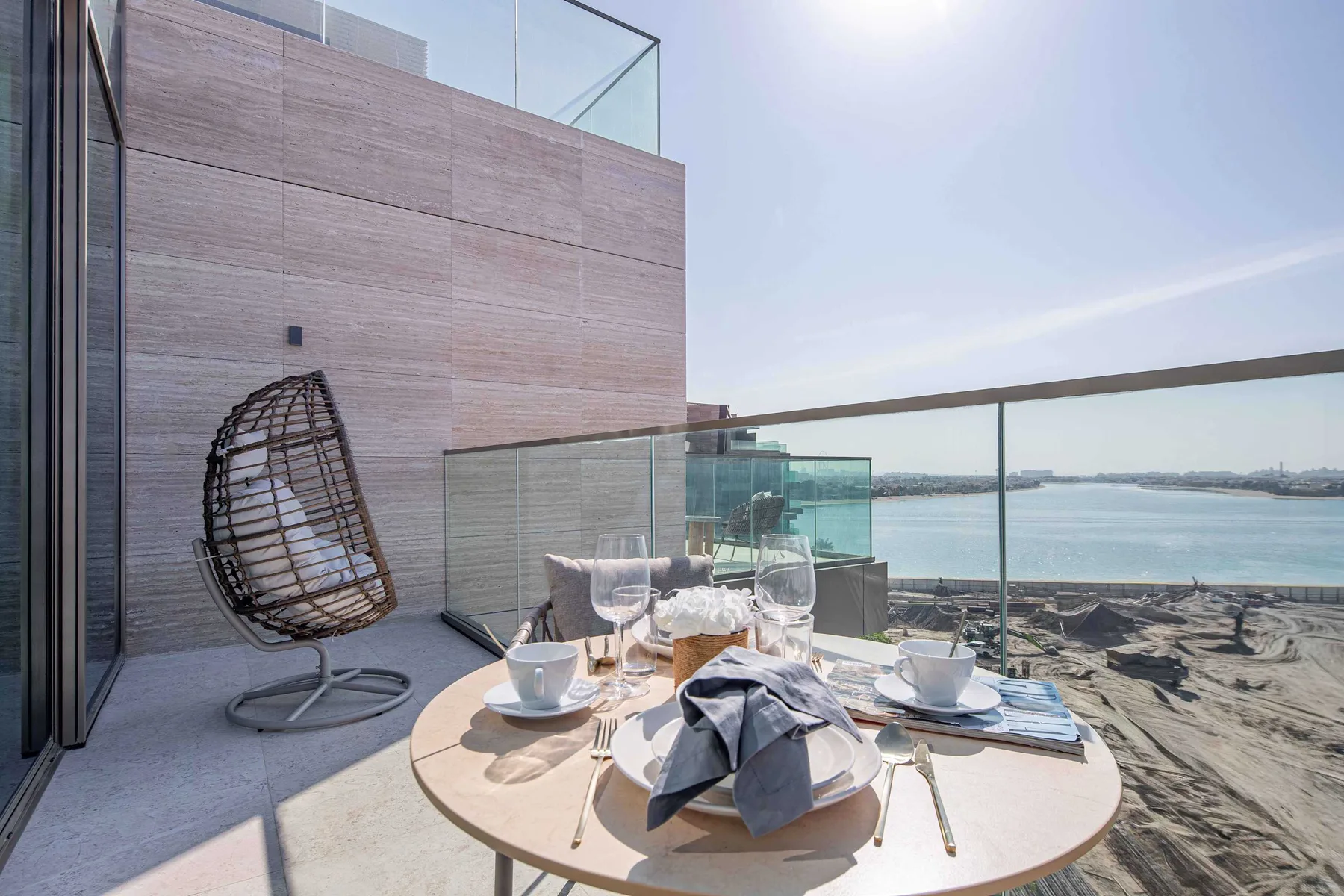 Una zona de comedor al aire libre da al agua, con una mesa puesta junto a una silla colgante.