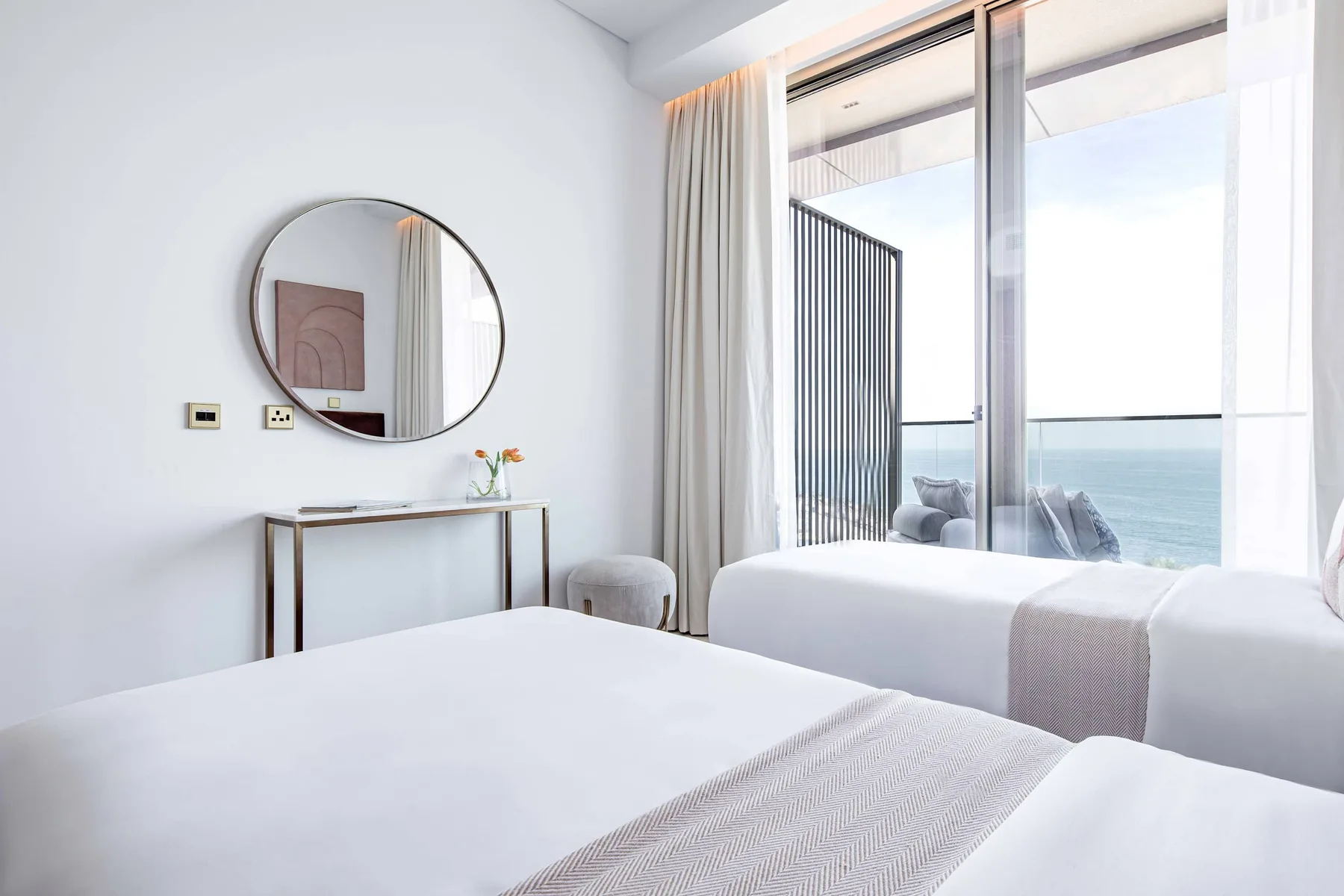 Un dormitorio luminoso con dos camas y una gran ventana con vistas al mar.