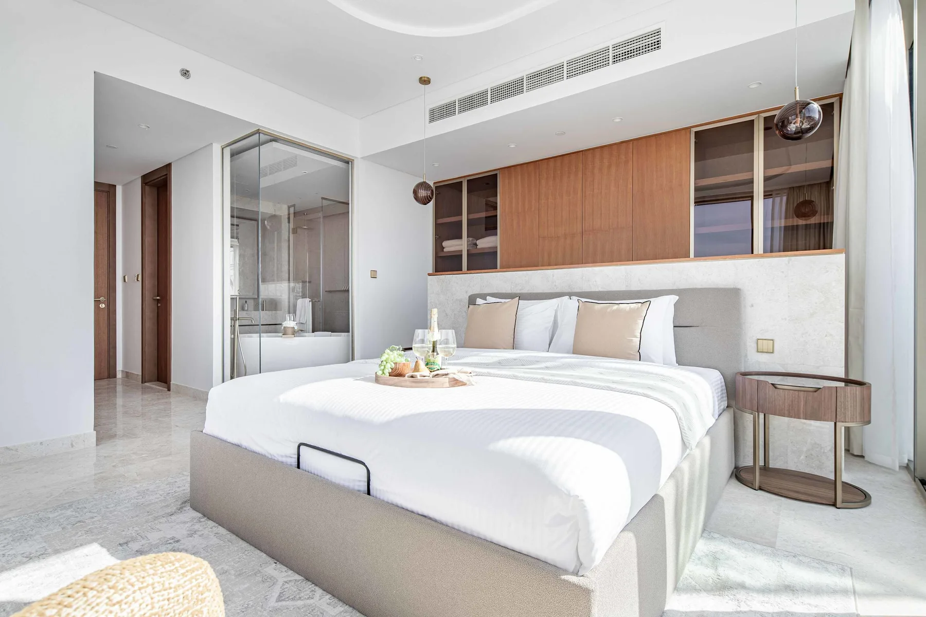 Un dormitorio luminoso con una cama bien tendida y un baño con paredes de vidrio.