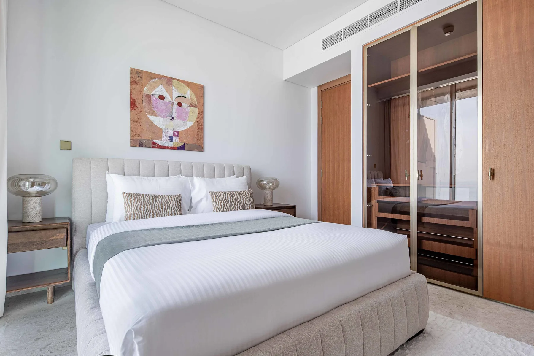 Un dormitorio con una cama tendida y una obra enmarcada encima.