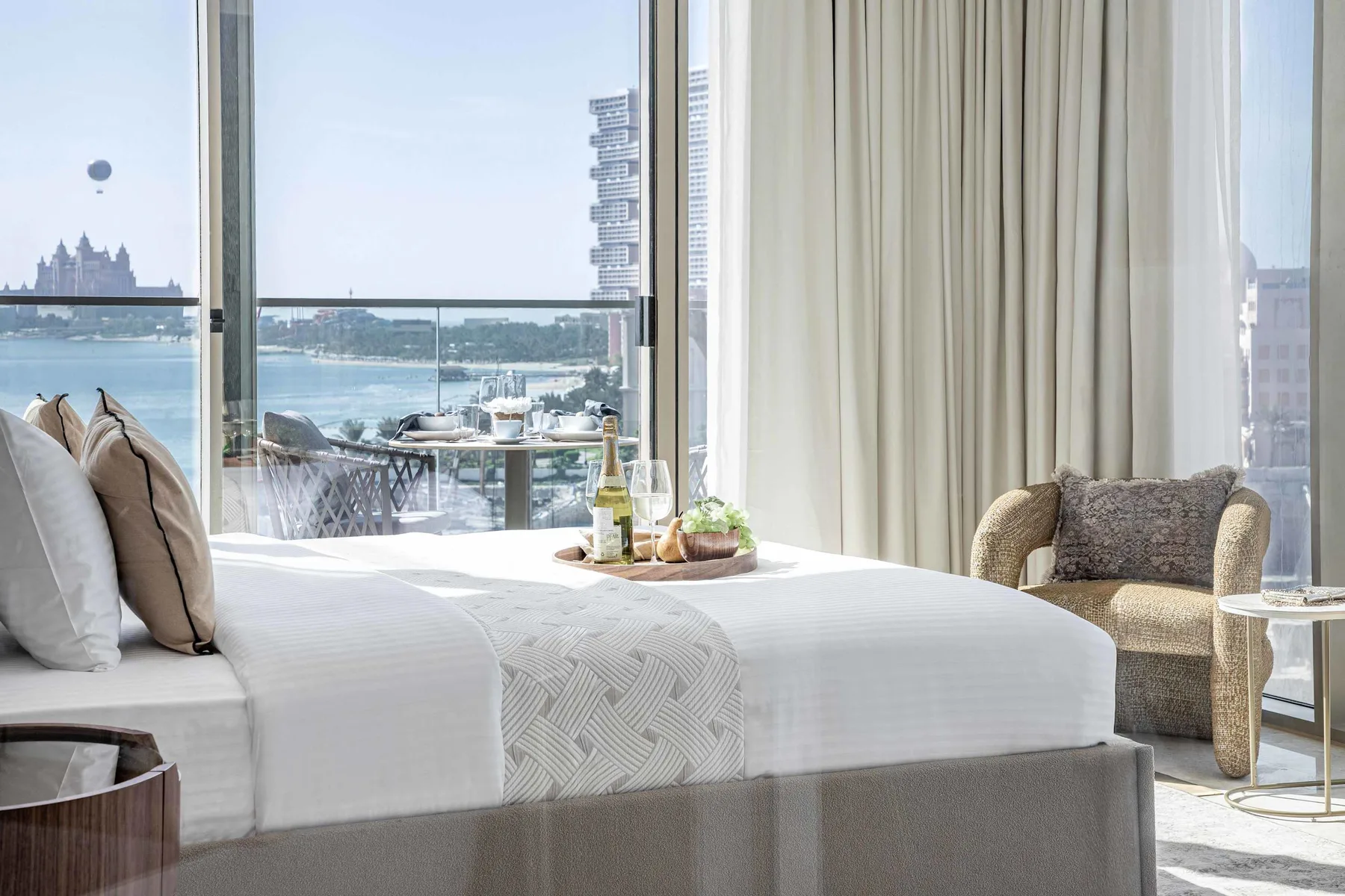 Un dormitorio luminoso con una cama bien arreglada junto a grandes ventanales con vistas al agua.