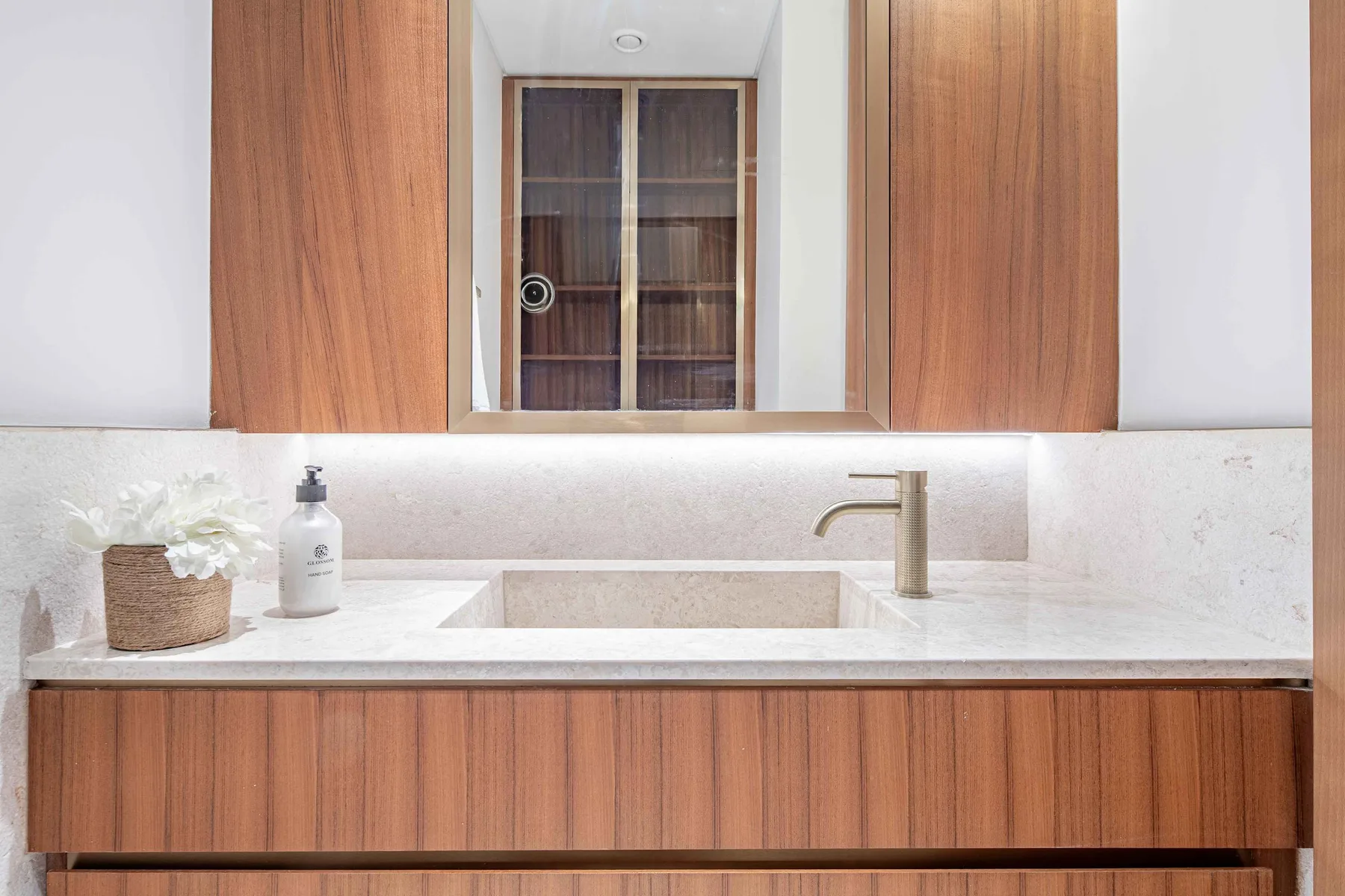 Un tocador de baño con lavabo blanco, gabinetes de madera y un espejo.