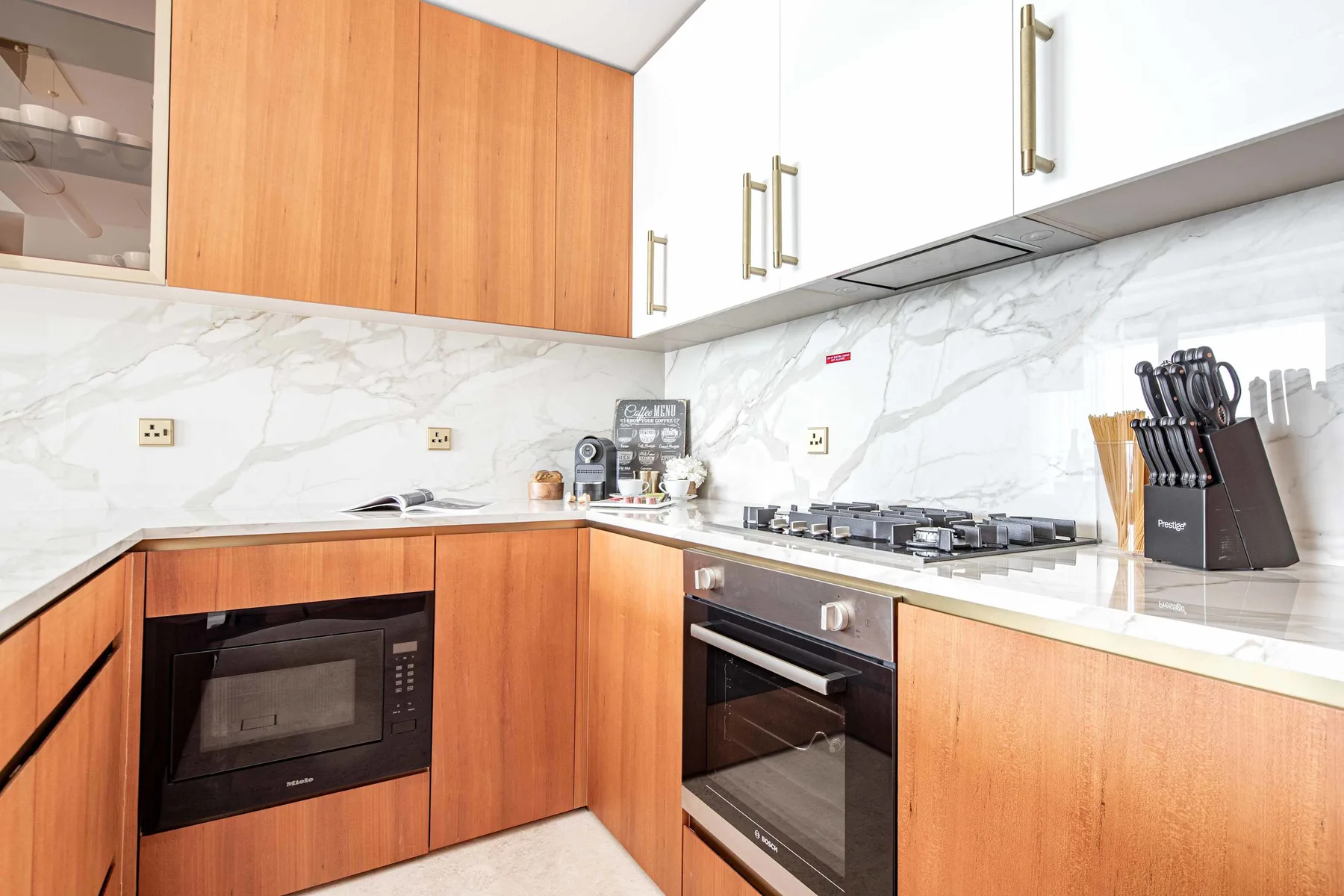 Una cocina moderna con gabinetes de madera, encimeras blancas y electrodomésticos integrados.