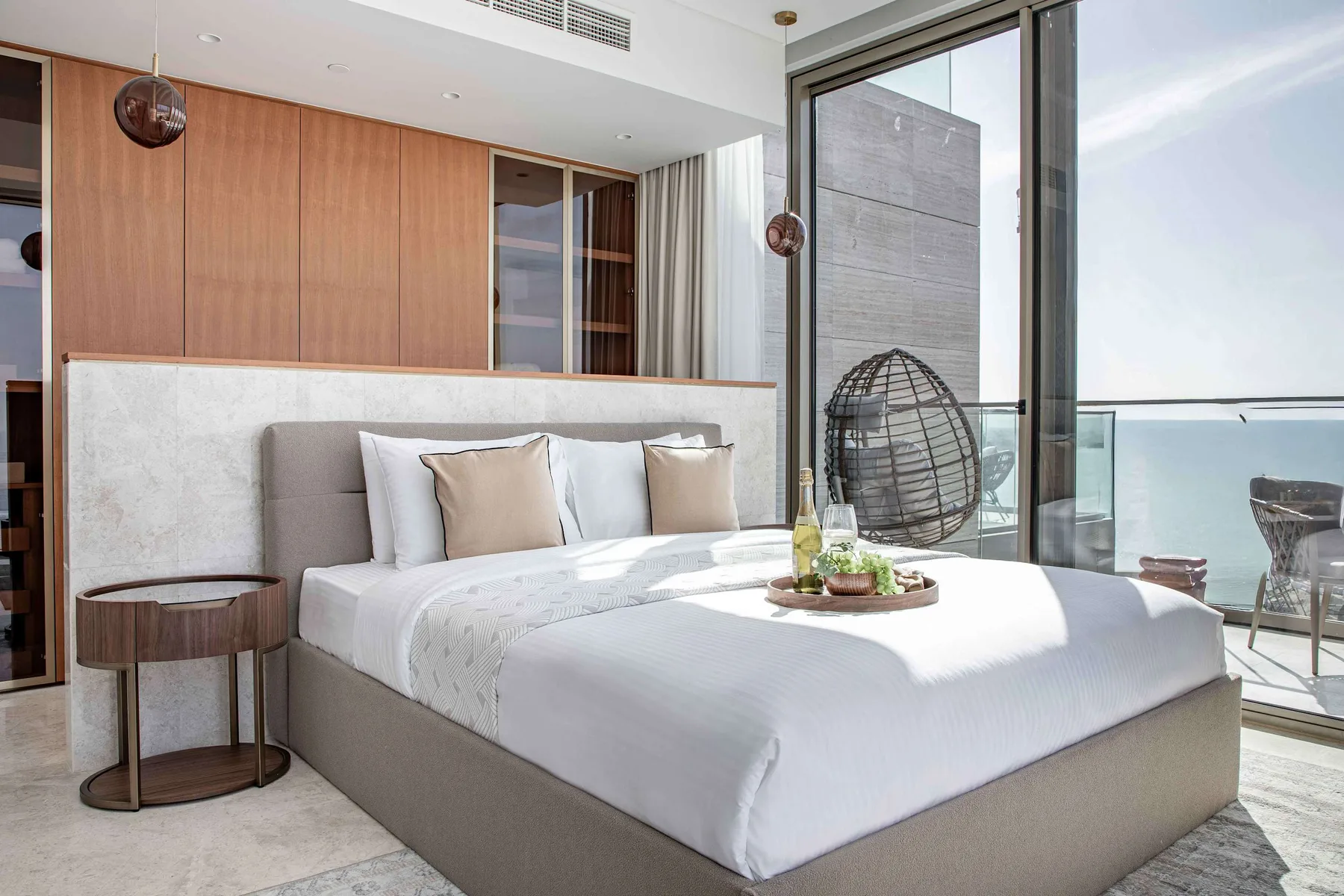 Un dormitorio luminoso con una cama bien tendida junto a ventanas de suelo a techo.