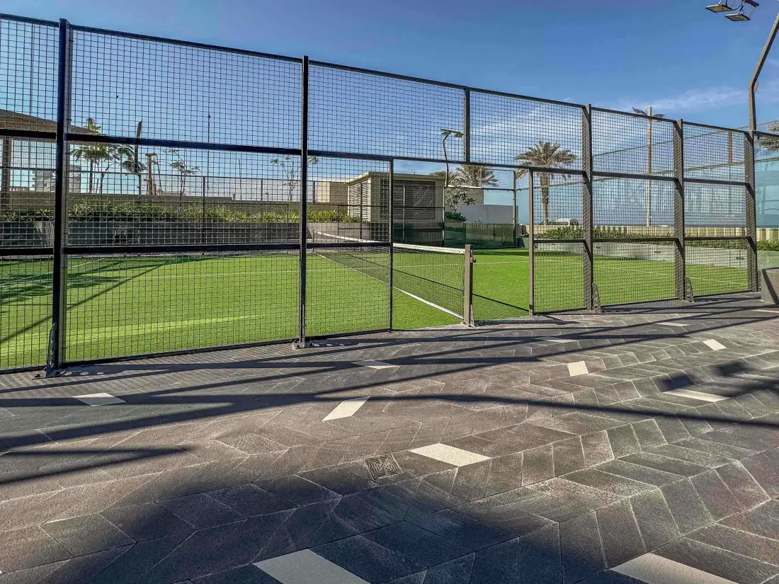 Una cancha deportiva al aire libre está rodeada por una alta valla de malla.