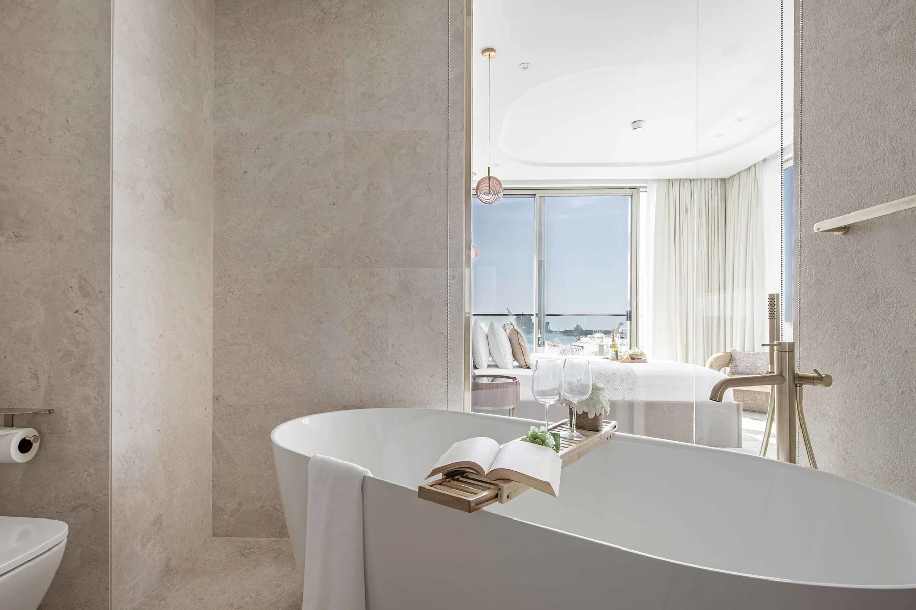 Un baño con una bañera exenta con vistas a un dormitorio luminoso.