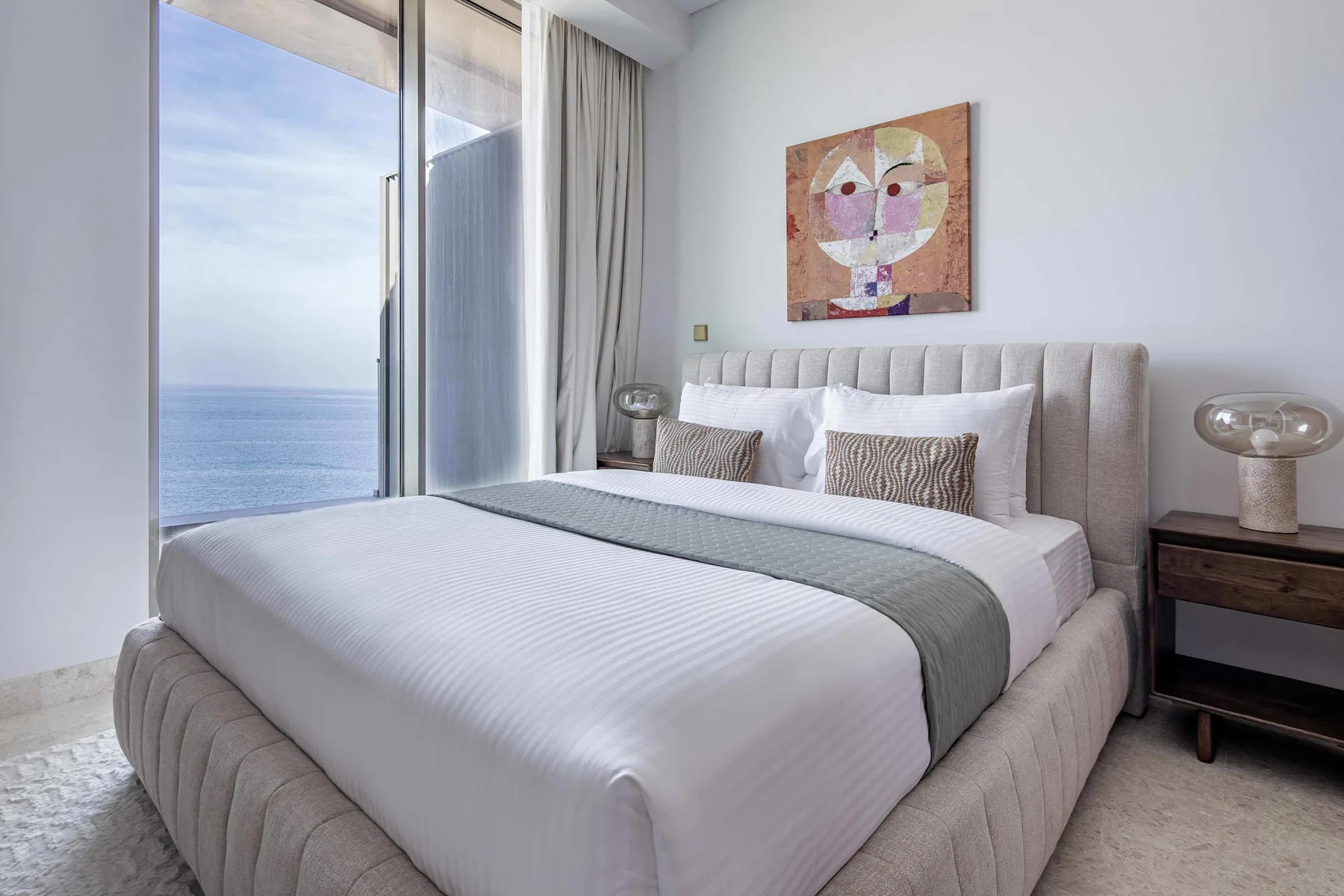 Un dormitorio con una cama tendida, una obra de arte y vistas al mar.