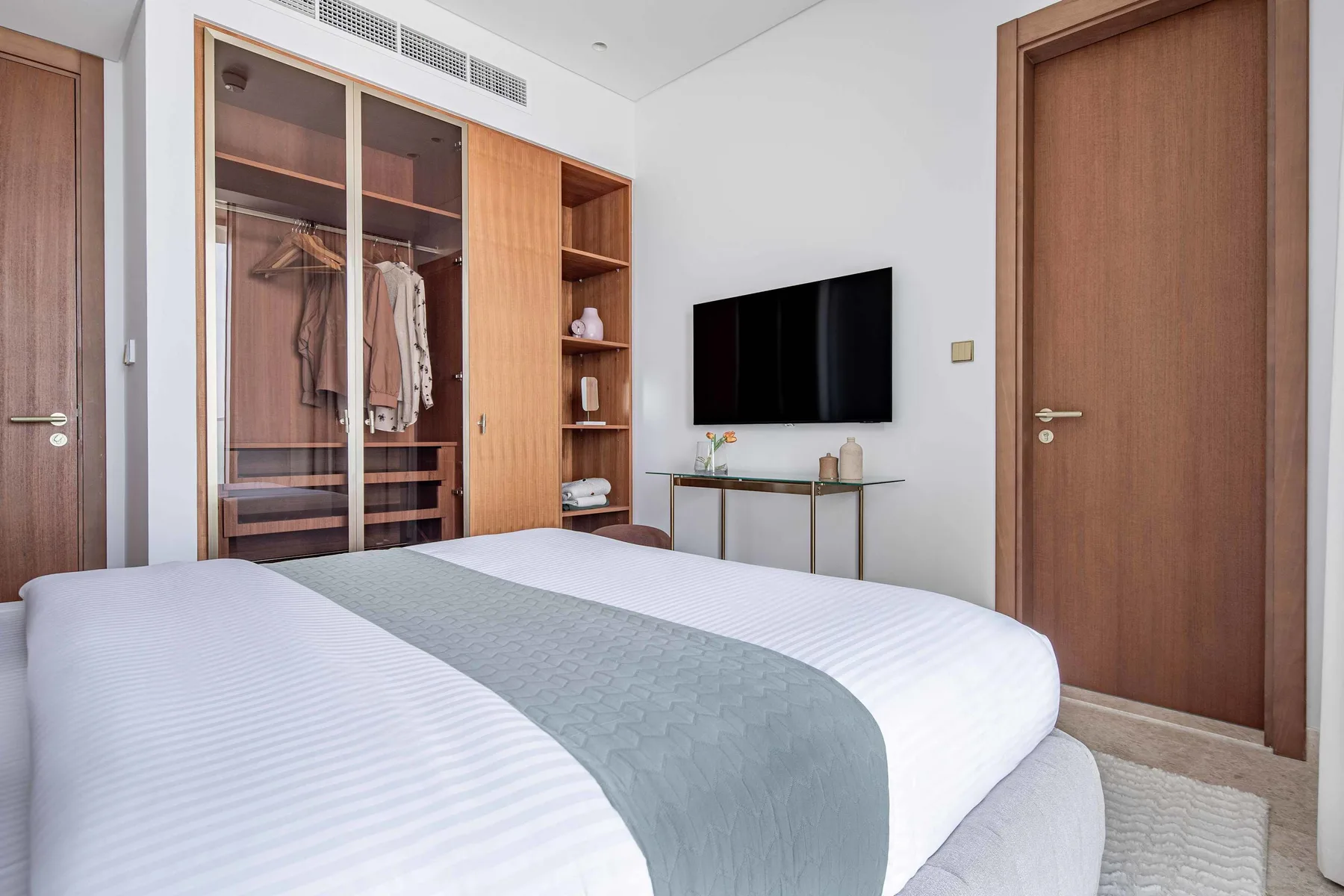 Un dormitorio con una cama bien tendida, un armario y un televisor en la pared.