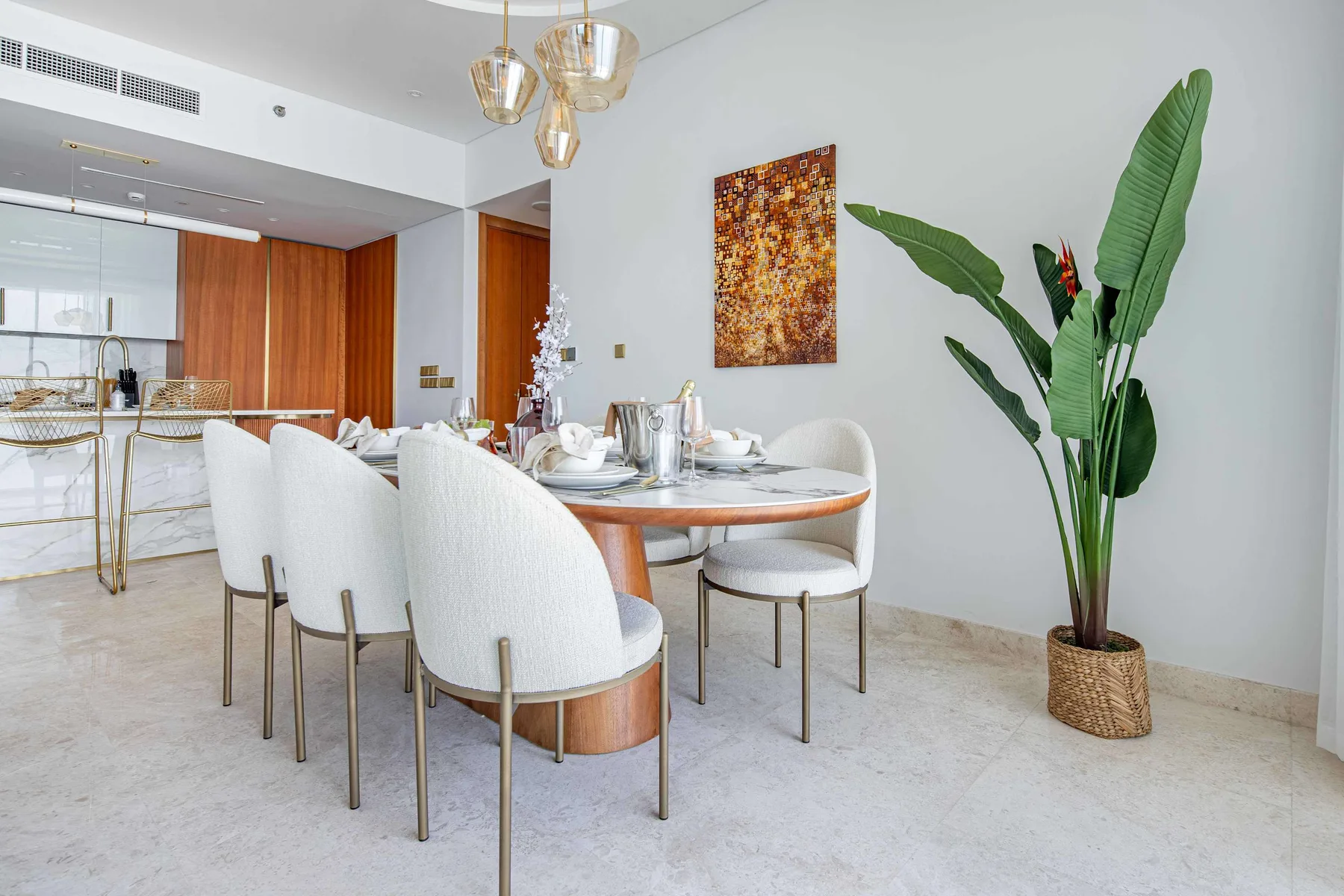 Un comedor con la mesa puesta, asientos blancos y una gran planta en maceta.