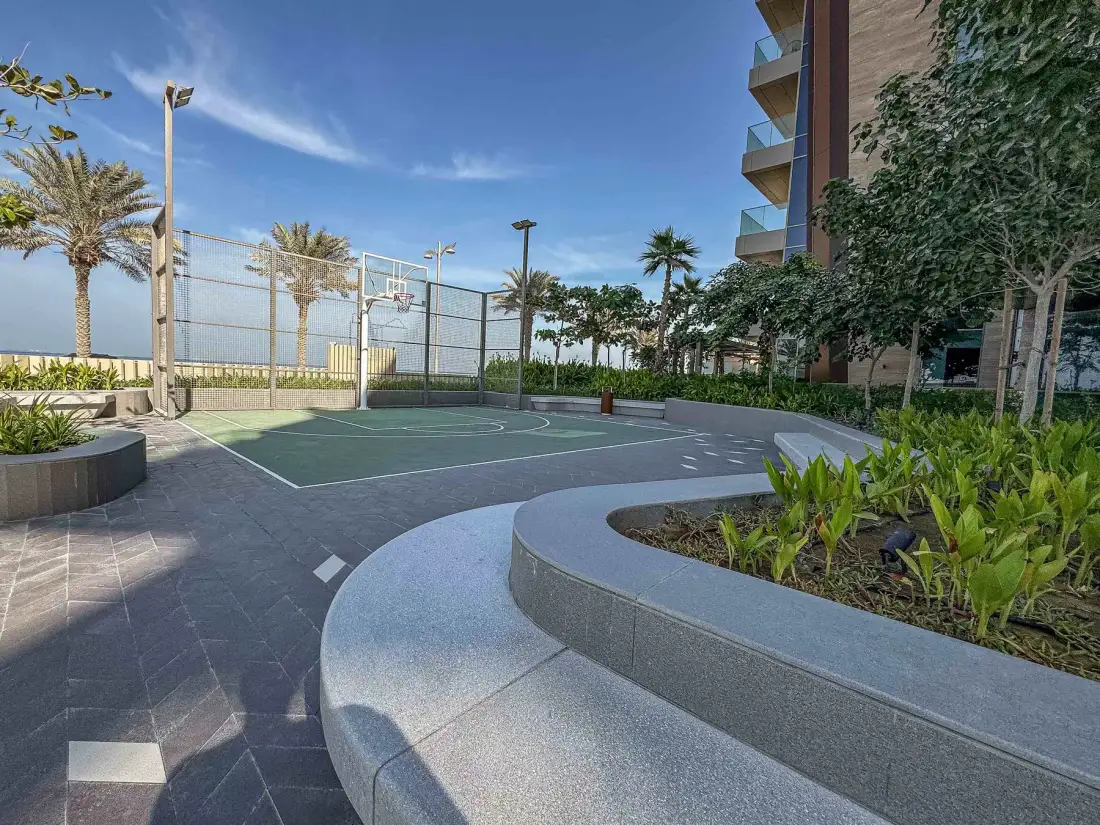 Una cancha de baloncesto al aire libre está junto a asientos curvos y jardineras.