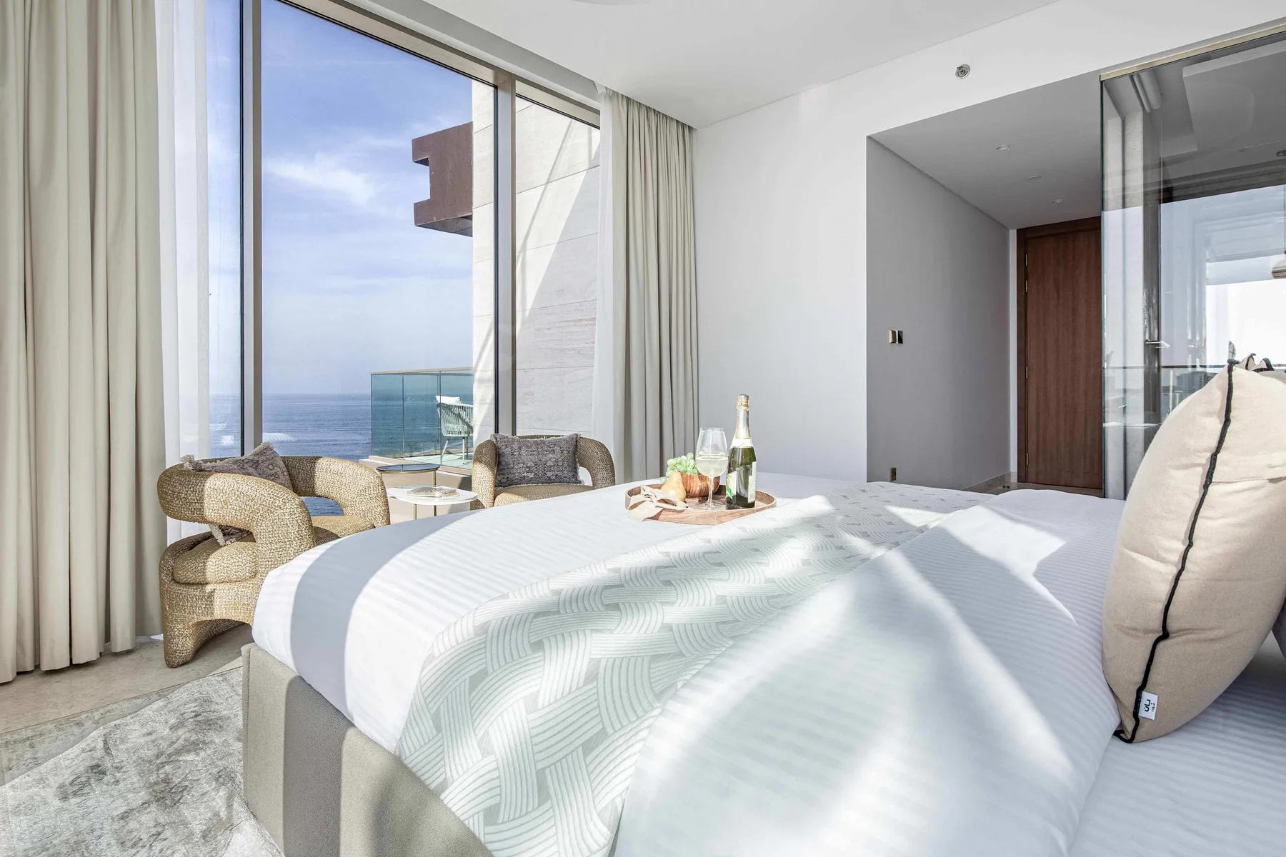 Un dormitorio luminoso con una cama tendida junto a grandes ventanas con vistas al mar.