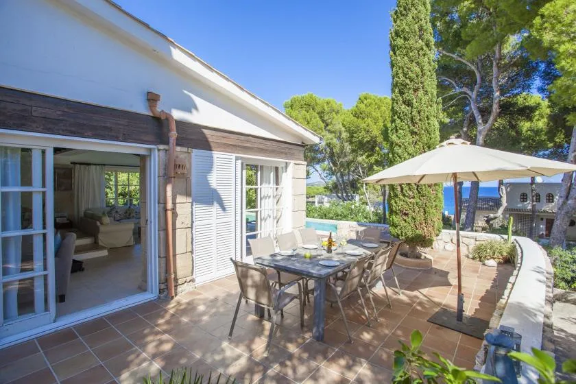A sunny patio with outdoor seating and a large umbrella beside the house.