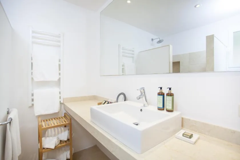 A bright bathroom vanity features a wide sink, wall mirror, and folded towels.