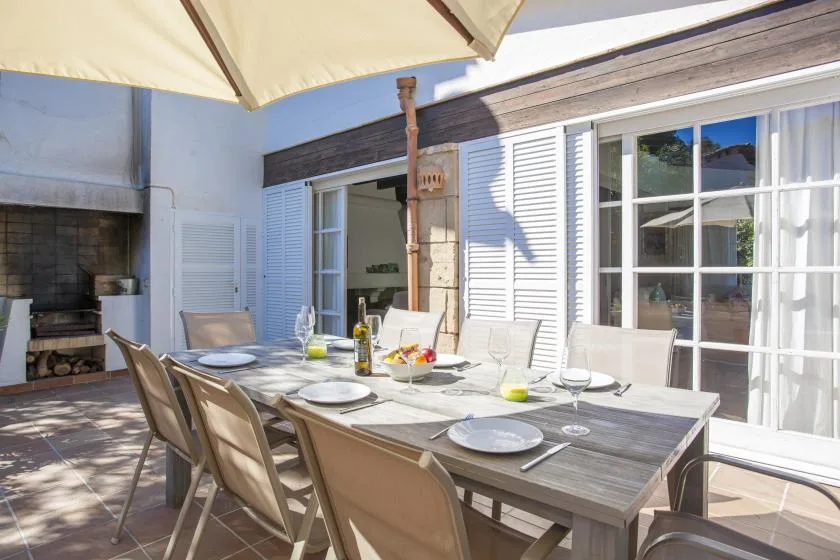 A sunlit outdoor dining area with a set table beneath a large umbrella.