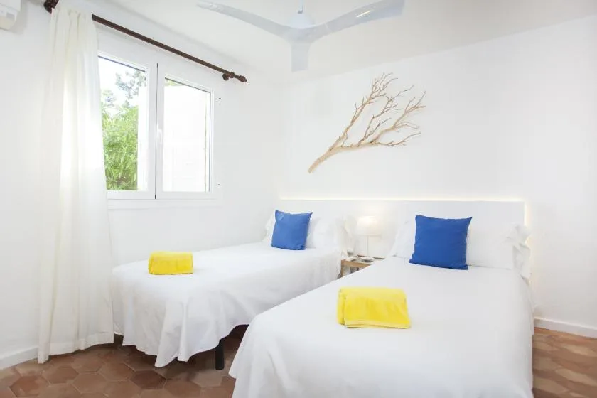 A bright bedroom with two beds dressed in white linens and blue pillows.