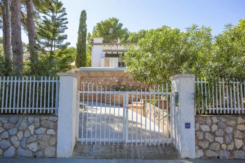 A gated property entrance with a stone wall and leafy trees.